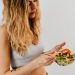 A caucasian woman in a sports bra enjoying a fresh salad, embodying healthy eating and lifestyle.