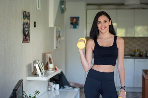 Smiling woman in activewear lifting dumbbells at home for a healthy lifestyle.